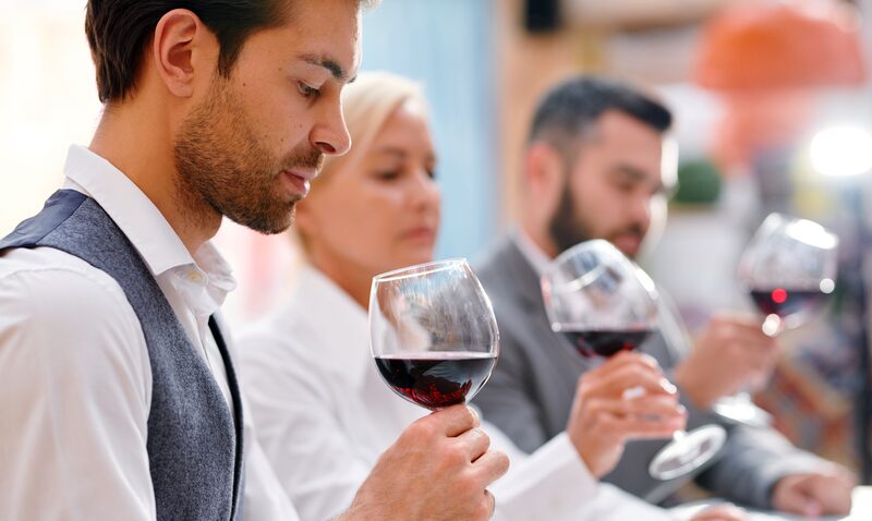 Mann prüft ein Glas Rotwein bei einer Weinprobe